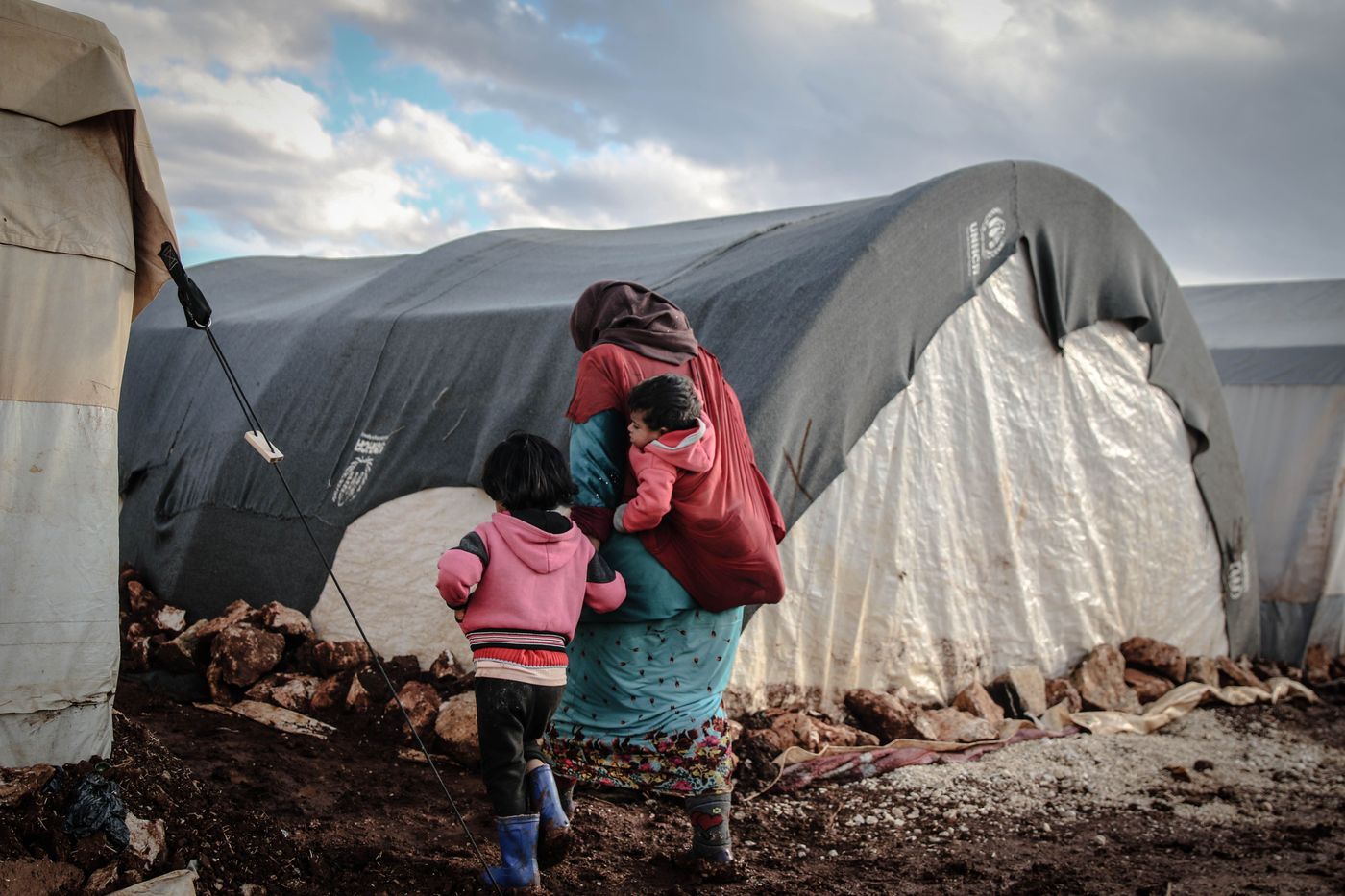 Illustrative photo: a mother and her children, seen from behind, at a displacement site